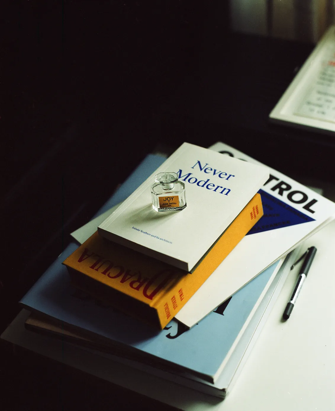 A stack of books including Never Modern and Dracula with a perfume bottle resting on top