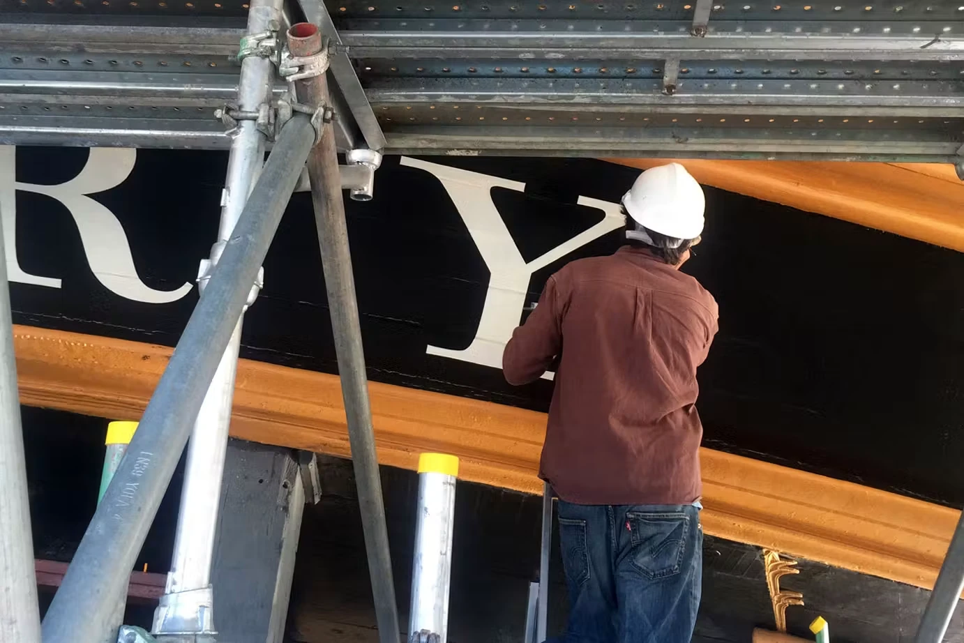 A painter applying large serif lettering to the stern of HMS Victory during restoration